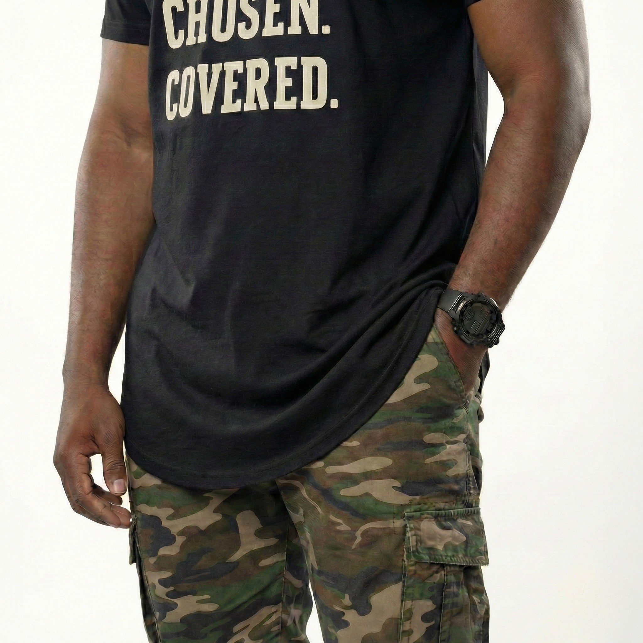 Person wearing a black t-shirt with 'CHosen. COVERED.' text and camouflage pants on a white background