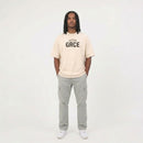 Person wearing a cream t-shirt with 'GRCE' logo and gray pants on a white background
