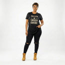 Woman wearing a black t-shirt with text, black pants, and tan boots on a white background