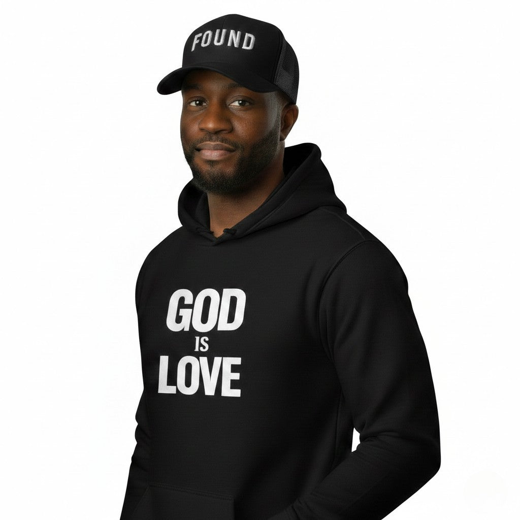 Person wearing a black hoodie with 'GOD IS LOVE' text and a black cap with 'FOUND' text on a white background