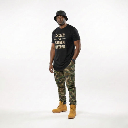 Man wearing a black t-shirt with text, camouflage pants, and yellow boots on a white background
