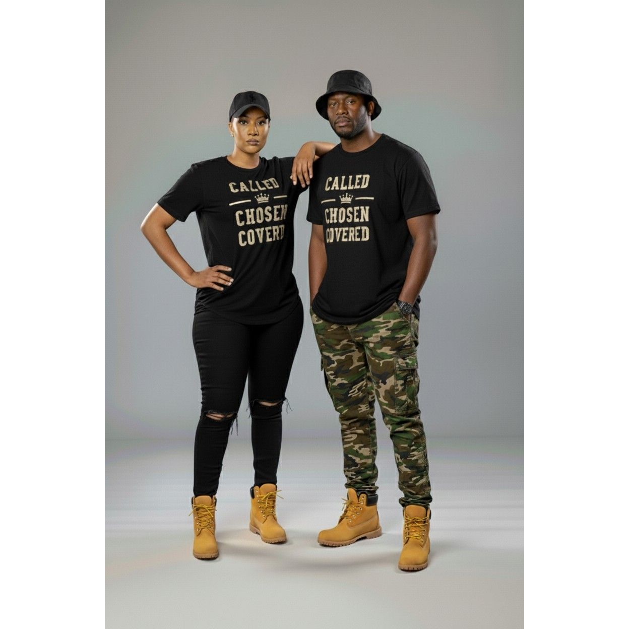 Two people wearing matching black t-shirts with text, standing against a gray background.