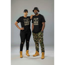 Two people wearing matching black t-shirts with text, standing against a gray background.