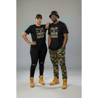 Two people wearing matching black t-shirts with text, standing against a gray background.