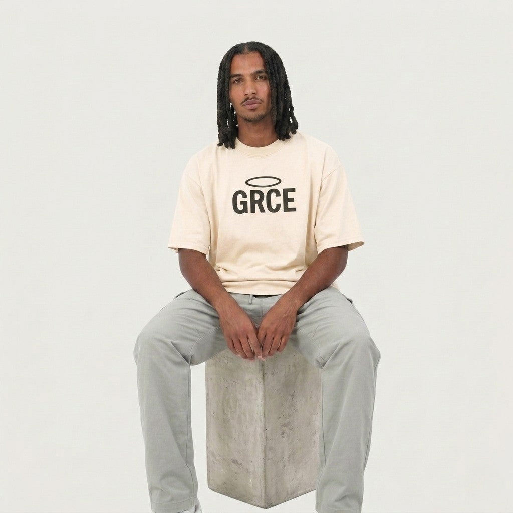 Person wearing a cream t-shirt with 'GRCE' logo sitting on a concrete block against a plain background