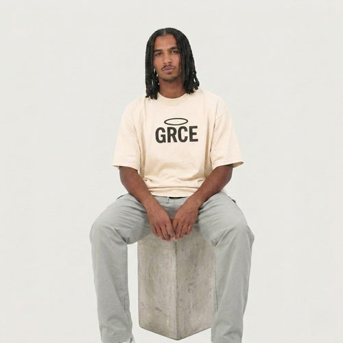 Person wearing a cream t-shirt with 'GRCE' logo sitting on a concrete block against a plain background