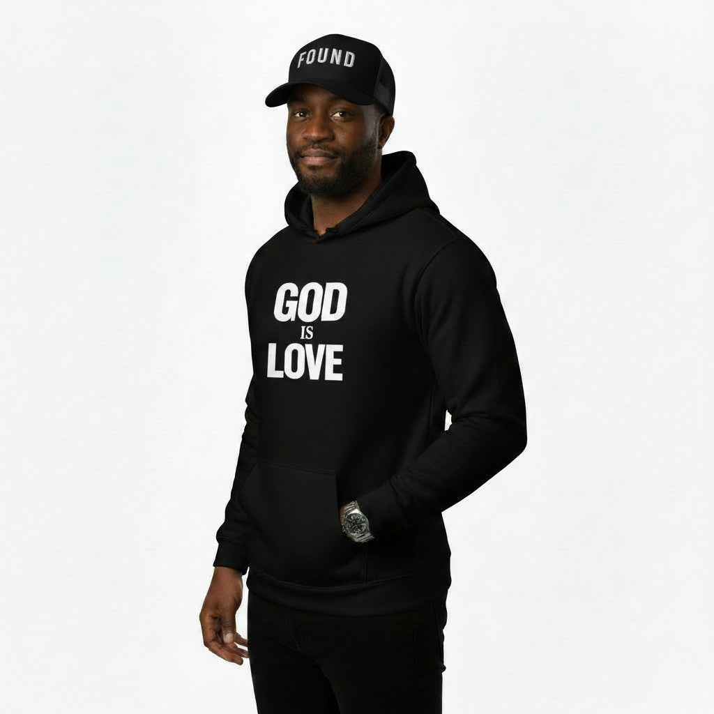 Person wearing a black hoodie with 'GOD IS LOVE' text and a matching cap on a white background